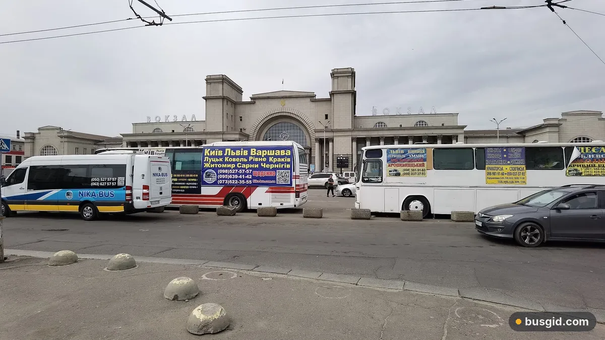 Головний залізничний вокзал Дніпра з високою аркою, на привокзальній площі стоять міжміські автобуси й мікроавтобуси