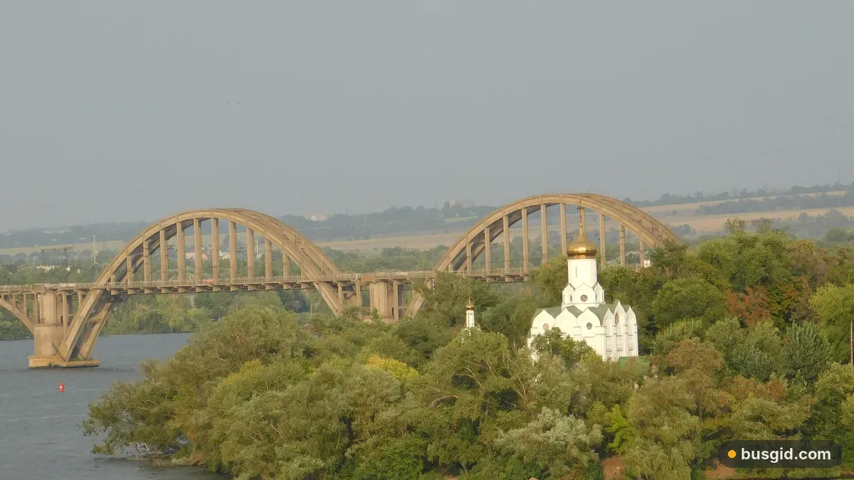 Монастирський острів у Дніпрі: біла церква з золотою банею серед зелені й арки Мерефо-Херсонського мосту над річкою