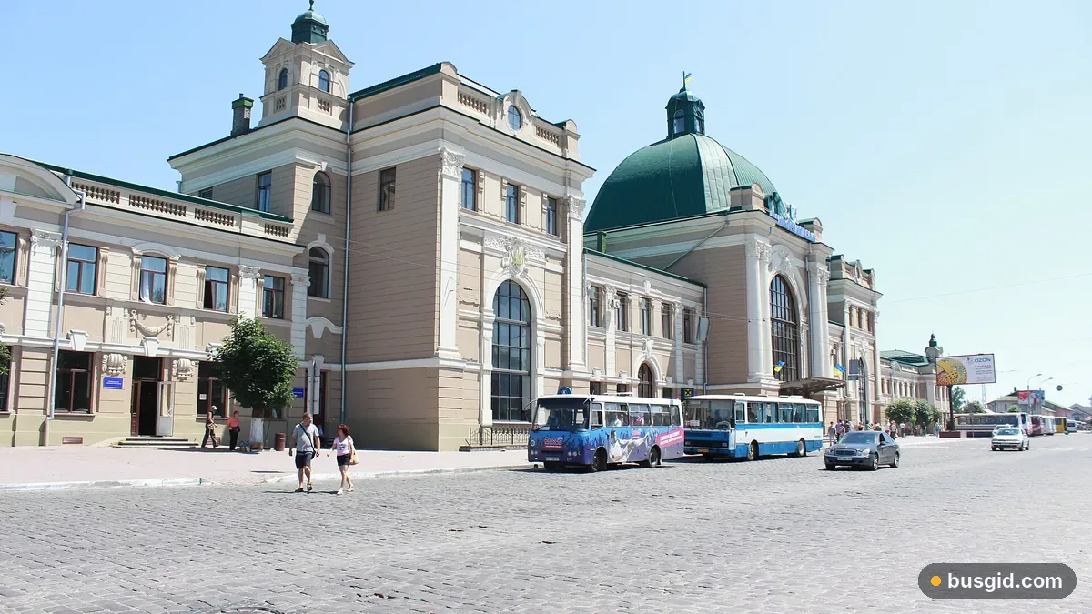 Залізничний вокзал Івано-Франківська з зеленим куполом на Привокзальній площі, поруч стоять міські автобуси