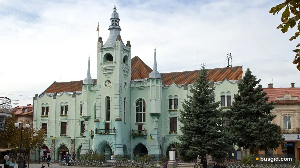 Бірюзова будівля ратуші Мукачева з годинниковою вежею та шпилями, перед нею ялинки на площі в центрі міста