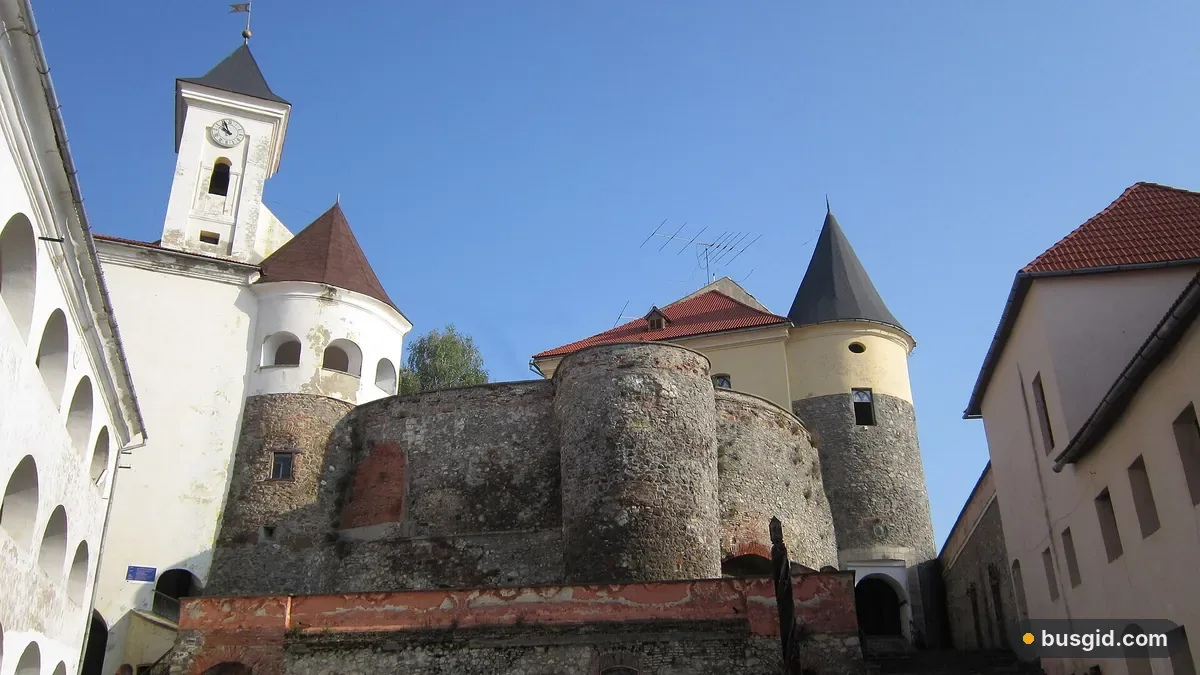 Подвір'я замку Паланок у Мукачеві: кам'яні круглі бастіони з конусними дахами та біла вежа з годинником