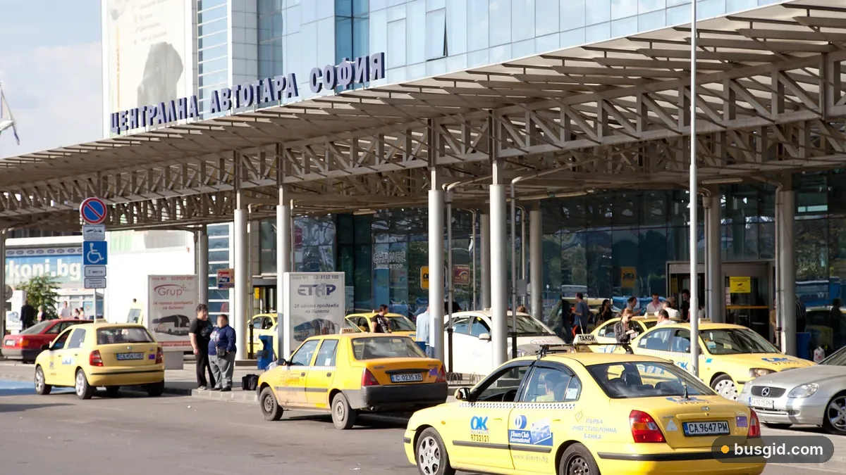 Вход в Центральный автовокзал Софии под металлическим навесом, у стеклянного фасада стоят жёлтые такси